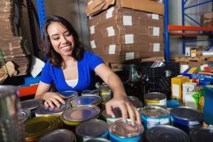 Young mixed-race woman sorting donated groceries in food bank warehouse