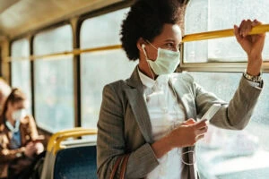 woman with face mask texting on the phone while traveling by bus.