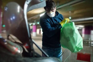 Man in mask and rubber gloves putting products in car after shopping
