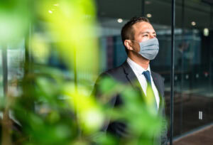 man in suit wearing medical mask, looking out office window