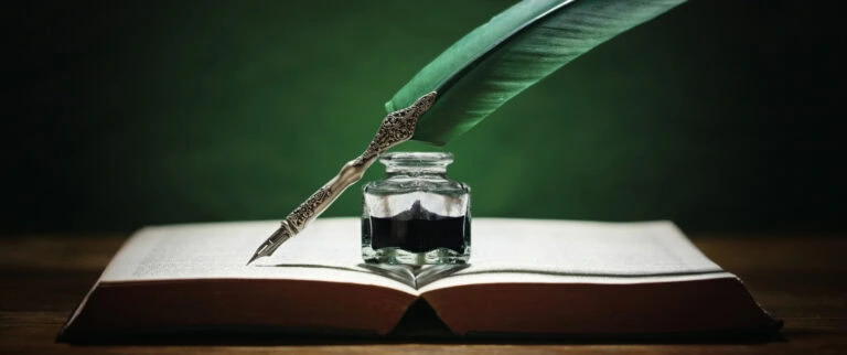 Quill pen and inkwell resting on an old book with green background concept for literature, writing, author and history
