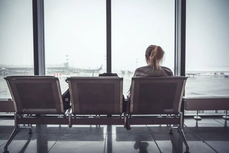 Stock photo of woman sitting at an airport terminal looking out a window at departing flights