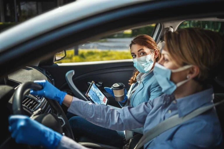 Stock photo of two women in a car, wearing masks and rubber gloves