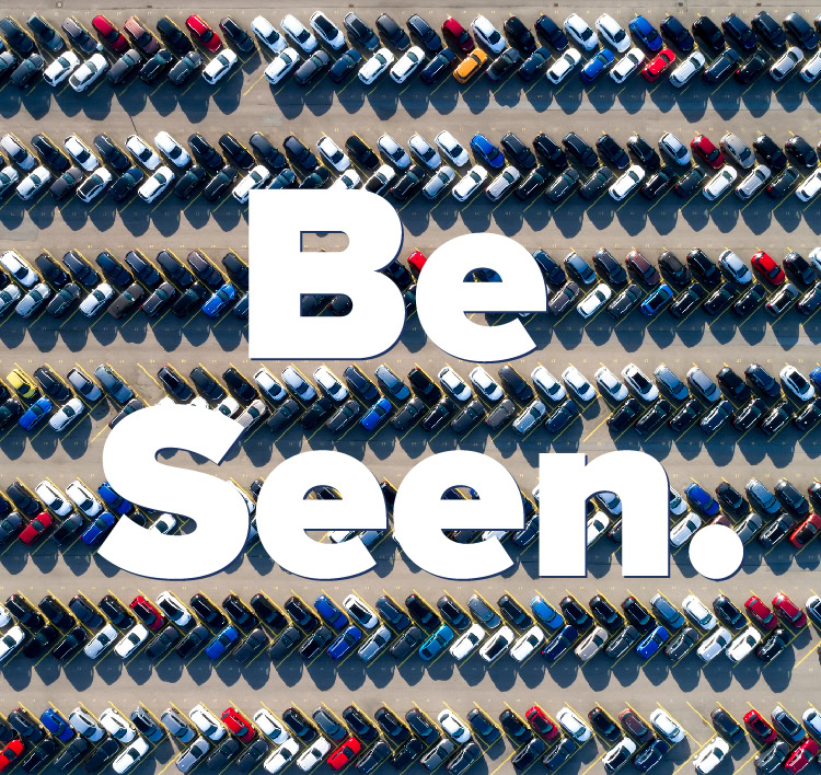 "Be Seen." in the foreground with aerial shot of many parked cars in the background