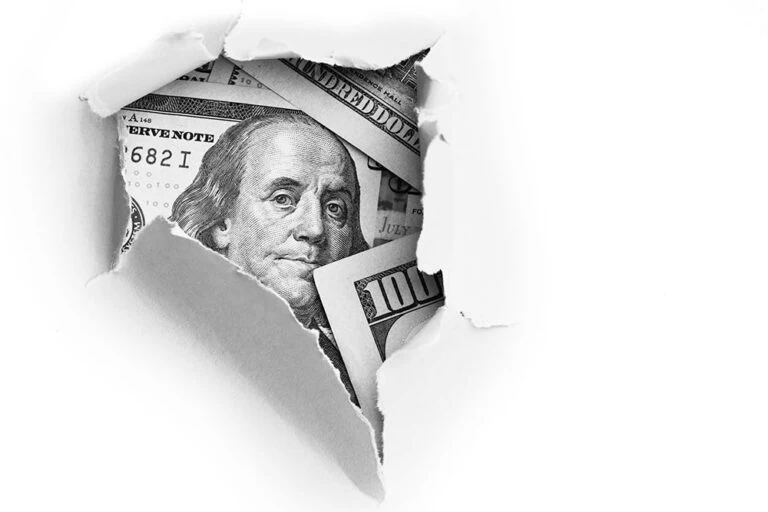 Hundred dollar bills shown through a hole in a sheet of paper