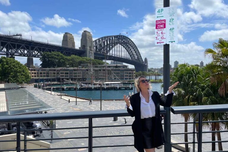Woman standing up against a railing in front of a bridge and palm trees