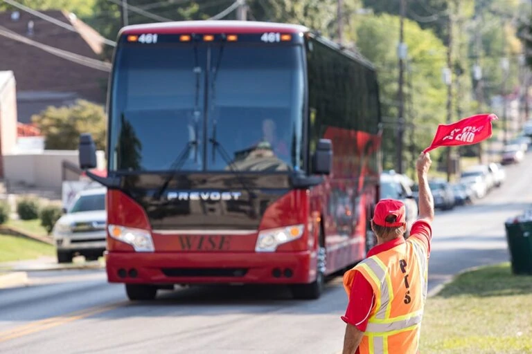 Large red bus traveling on a street with a crossing guard