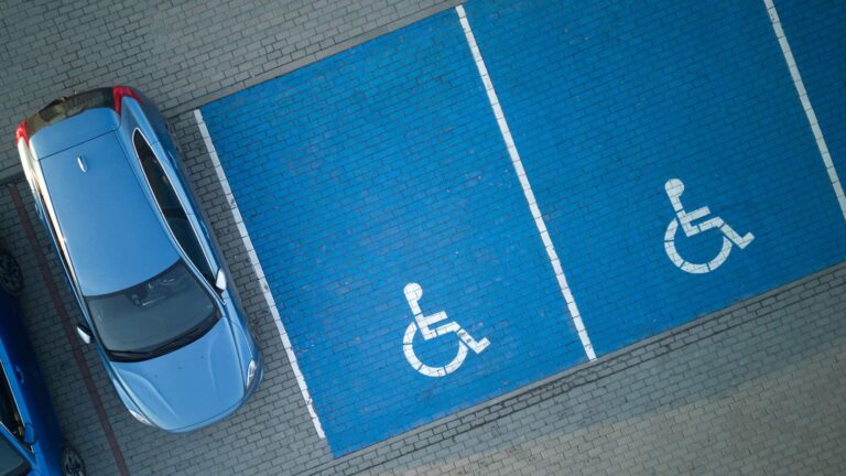 Blue car in a parking space next to 2 handicapped parking spaces