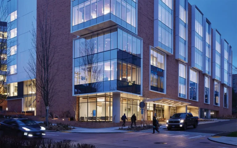 Lit up office building at dusk with pedestrians working towards doors