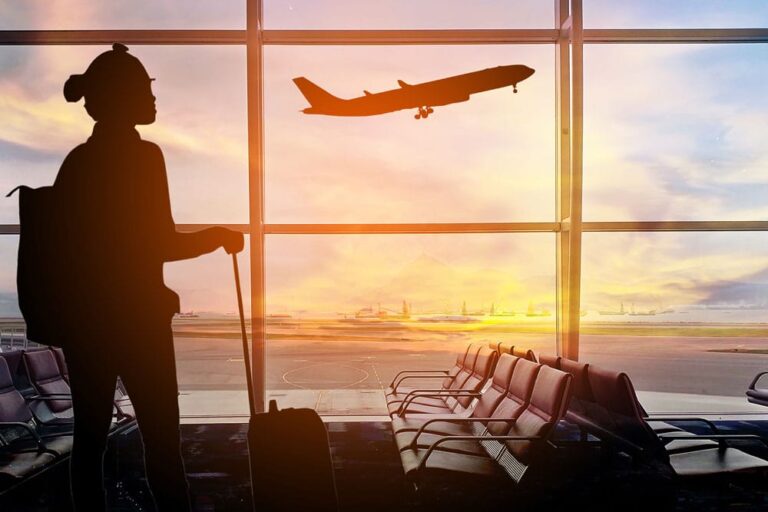Silhouette of a woman with a suitcase in an airport watching a plane take off. Airline travel concept.