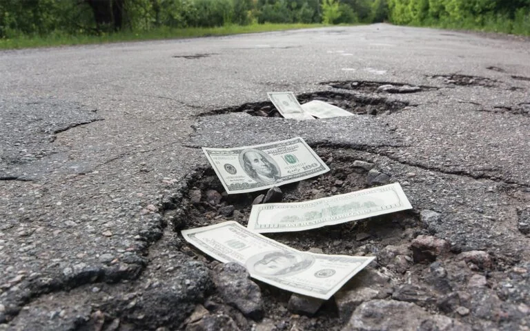 Stock photo of road potholes showing several 0 bills within each pothole.
