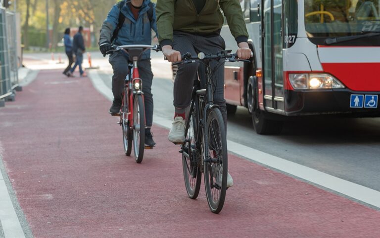 Two men riding bicycles on a sidewalk near a bus in the street