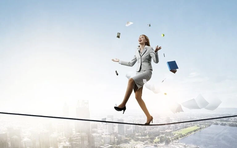 Young pretty businesswoman juggling business items while balancing on a tightrope over a city