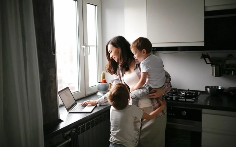 A busy mom with two children works on a laptop in the kitchen