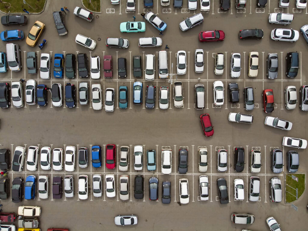 An aerial view of the lines of parked cars. Heavy traffic in the parking lot. Searching for spaces in the busy car park. Cruising for parking in dormitory area. Difficulties of parking in the city.