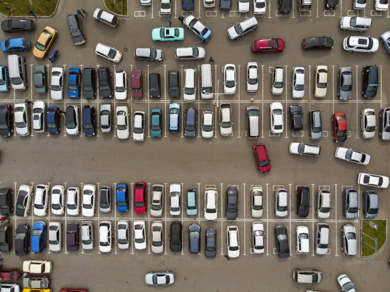 An aerial view of the lines of parked cars. Heavy traffic in the parking lot. Searching for spaces in the busy car park. Cruising for parking in dormitory area. Difficulties of parking in the city.