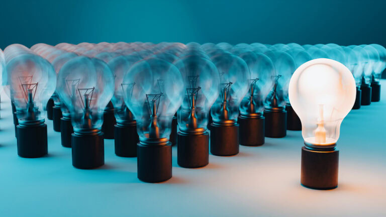 Group of light bulbs in rows, all of which are unlit except for one bulb which is glowing. The background is a gradient of blue, adding a cool tone to the scene. The glowing light bulb stands out prominently against the unlit bulbs, symbolizing concepts such as uniqueness, innovation, leadership, and standout ideas.