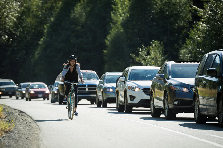 Woman commutes by bicycle past traffic, Whistler, B.C.