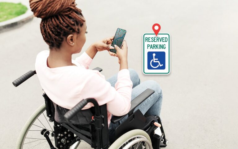 image of a woman sitting in a wheelchair looking at a map on her mobile phone, near a sign that says "Reserved Parking"