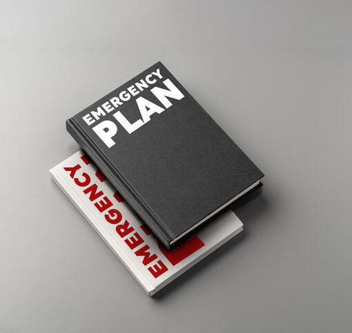 Two books about emergency plans are stacked on a gray surface, focused on preparedness.